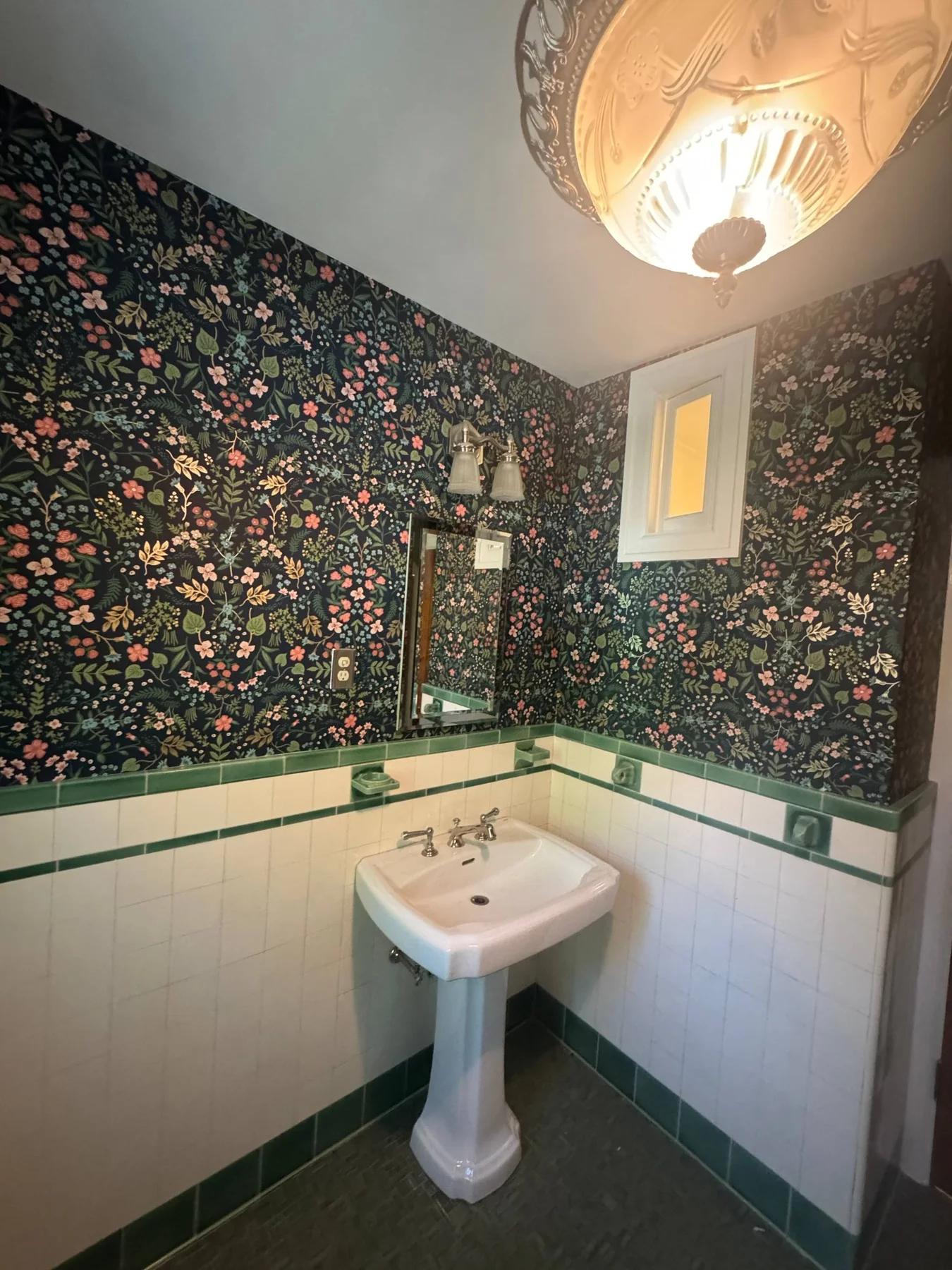 Small floral wallpaper above green and cream tile in a bathroom