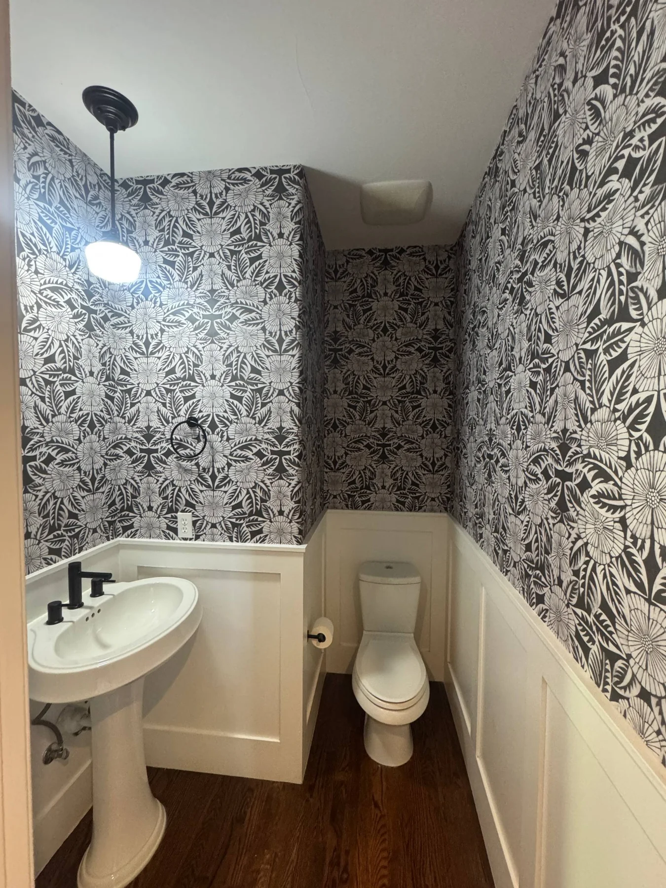 Black and white floral wallpaper above white wall panelling in a powder room