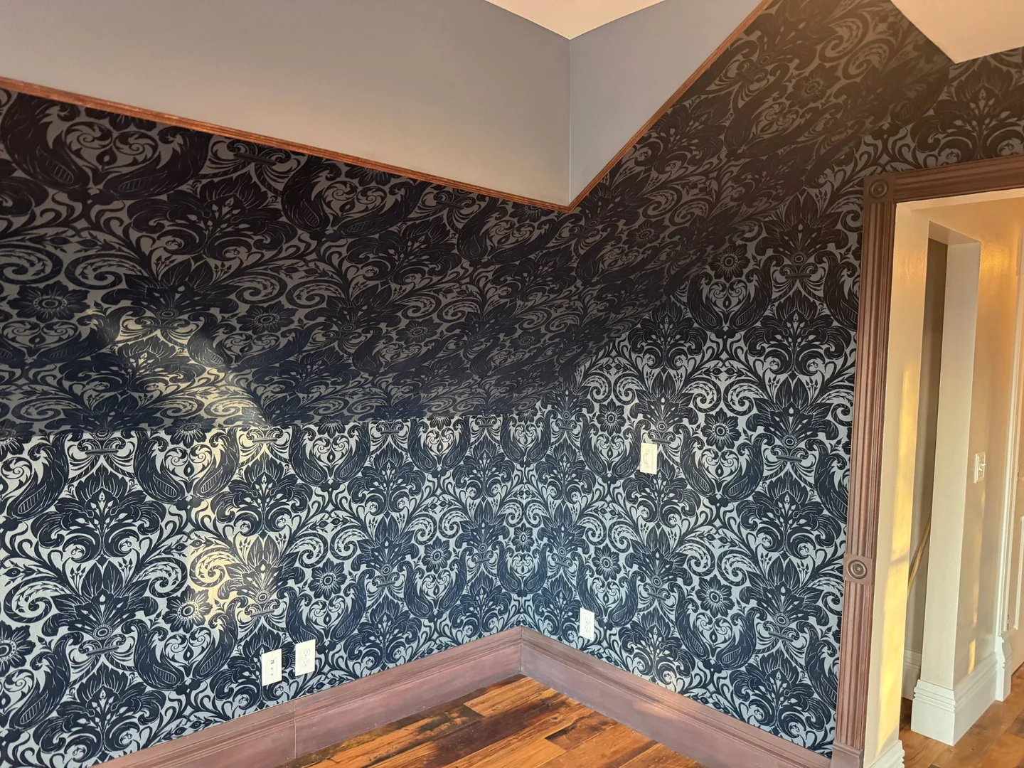 Dark ornamental wallpaper fitted around sloped ceilings and wood trim